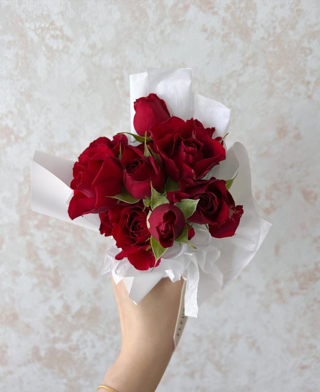 Pequeño ramo de rosas rojas con hojas verdes, sostenido en una mano