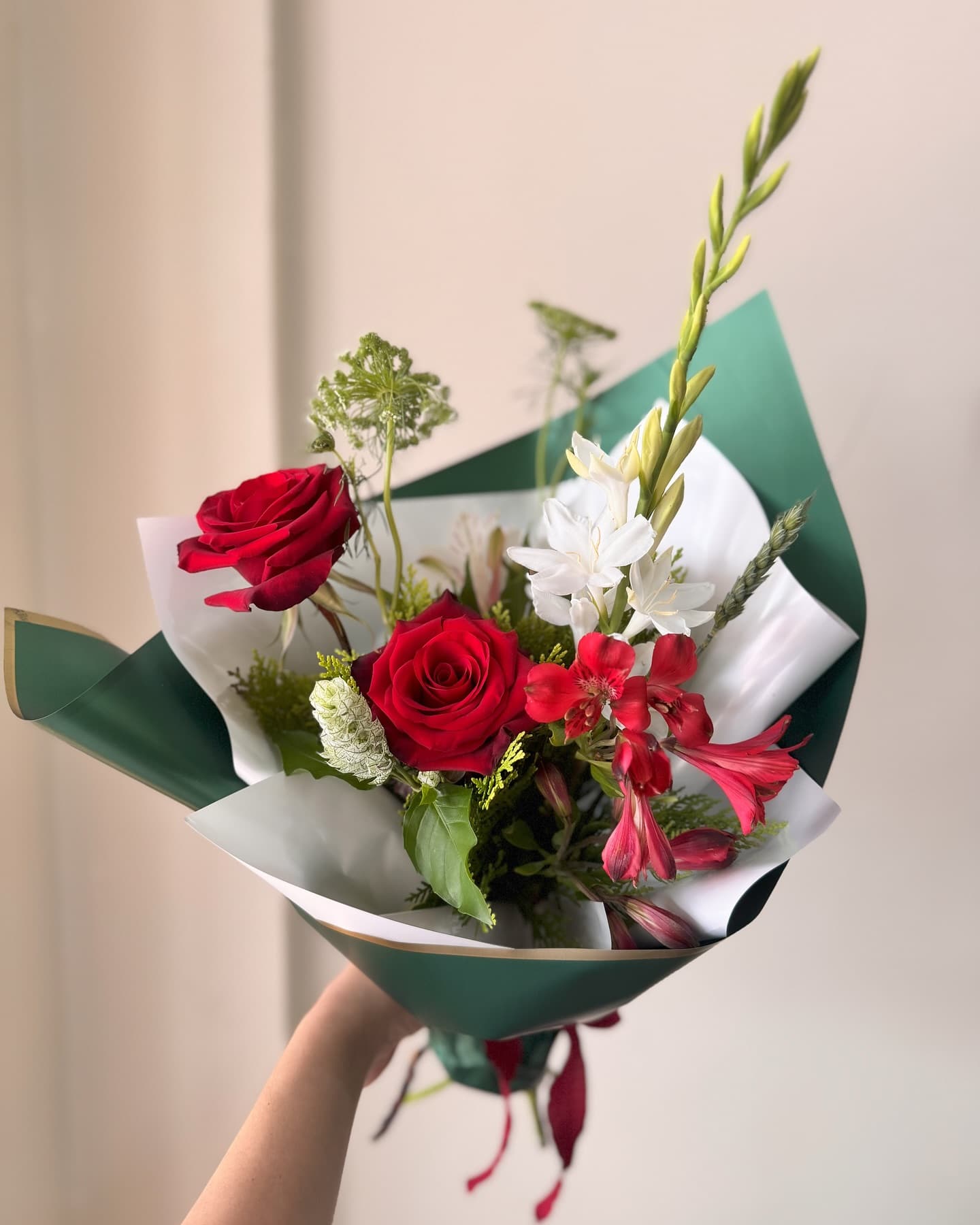 Ramo de rosas rojas envuelto en papel verde, sostenido en una mano